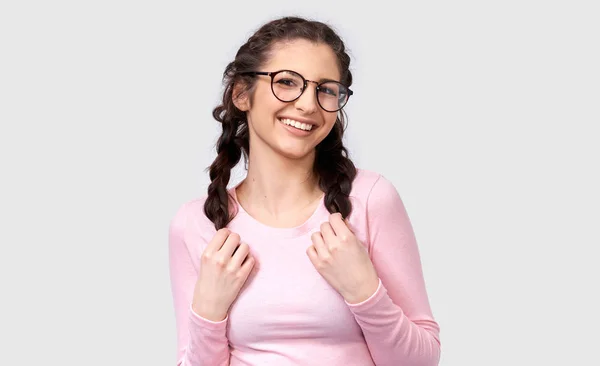 Studio portrait of pretty young woman smiling broadly, wearing casual outfit and round eyeglasses. Caucasian brunette female in pink blouse posing over white studio wall. People and emotions concept — Stock Photo, Image