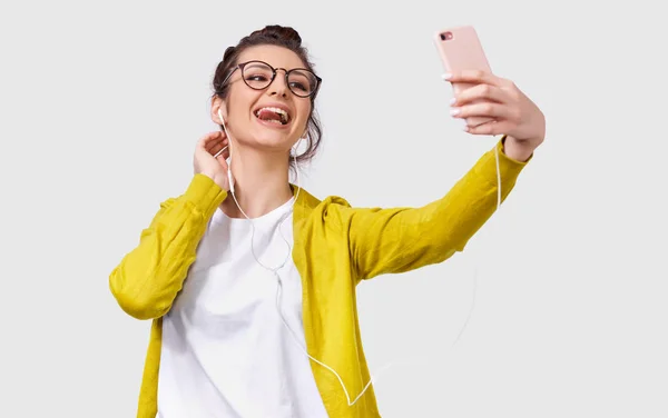 Jeune femme européenne en tenue décontractée debout et prenant un selfie isolé sur fond de studio blanc. Jolie femme caucasienne portant des lunettes transparentes faisant autoportrait — Photo