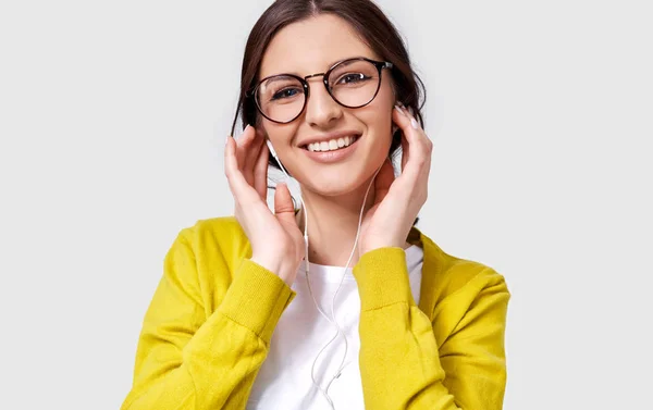 Foto close-up de uma jovem branca bonita sorrindo amplamente, ouvindo a música em fones de ouvido. Mulher feliz apreciando as músicas favoritas em fones de ouvido. Conceito de pessoas, música e tecnologia — Fotografia de Stock