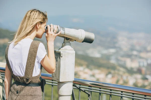 Immagine vista posteriore di una giovane donna che guarda attraverso un binocolo a moneta alla bellissima vista della città durante il suo viaggio. Viaggiatore femminile guardando attraverso il telescopio durante la giornata di sole in vacanza. Viaggio — Foto Stock