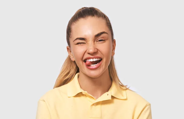Närbild porträtt av rolig ung blond kvinna gör roliga ansikten på kameran, sticker ut tungan. Positiva kvinnliga ha roligt, vilket gör grimas klädd i gul t-shirt. Människor och känslor — Stockfoto