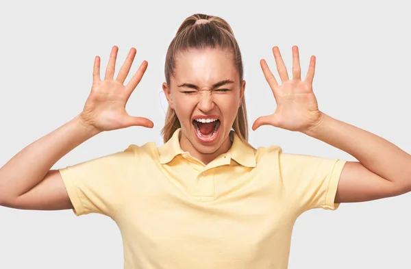 Mujer rubia asombrada gestos con ambas manos, gritando fuerte, vistiendo camiseta amarilla, posando sobre fondo blanco del estudio. Mujer triste caucásica sintiéndose enojada. Concepto de personas y emociones — Foto de Stock