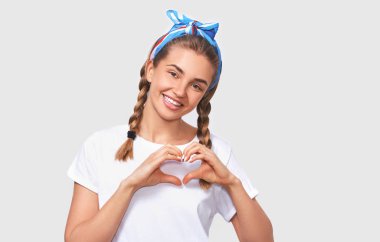 Samimi güzel genç kadın portresi geniş gülümseyen ve göğüs üzerinde kalp jesttutar, kameraya bakarak, beyaz tshirt giymiş, beyaz arka plan üzerinde. İnsanlar, duygular, vücut dili
