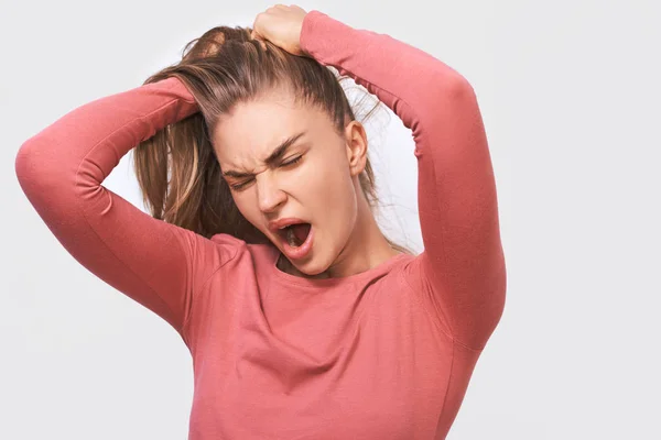 Closeup portrait of tired Caucasian young woman yawning, wearing pink blouse and round transparent eyewear, posing over white studio wall. Sleepy female with hair bun, feel sleepy. People and emotions