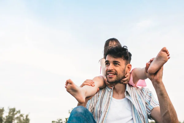 Jovem pai está passando tempo com sua pequena filha alegre ao ar livre. Imagem de menina bonita feliz brincando com o pai no parque durante o pôr do sol. Dia dos Pais. Papai e filha compartilha amor — Fotografia de Stock