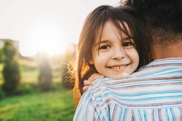 Image rapprochée de fille heureuse embrasse son père se sent joyeux. Joyeux petite fille mignonne jouant avec le père dans le parc, souriant et regardant vers la caméra. La fête des pères. Papa et fille partagent l'amour . — Photo