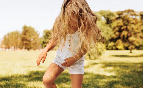 Imagem ao ar livre de sorrir adorável menina com longos cabelos loiros brincando no fundo da natureza. Criança feliz desfrutando da hora de verão no parque. Criança alegre tem atividade na floresta à luz do sol — Fotografia de Stock