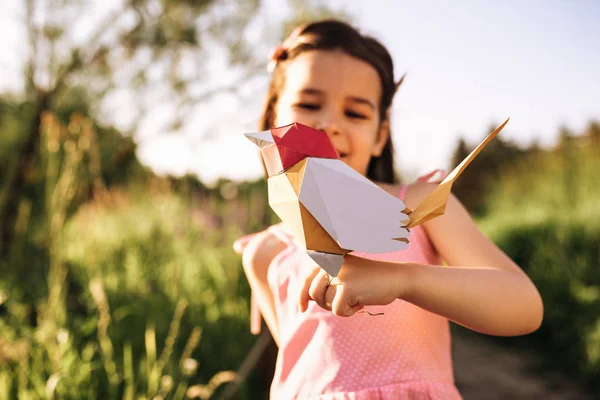 Lächelnd niedliches kleines Mädchen mit einem bunten Vogel aus Papier im Park. glückliches Kind, das mit einem Vogelspielzeug im Freien spielt. Umwelt- und Umweltkonzept. Kindheit. Kinder lernen, sich um die Natur zu kümmern — Stockfoto