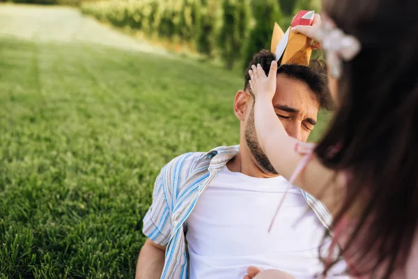 Rear view of child playing with her father with colorful bird toy sitting on the green grass outdoors. Cheerful daughter enjoying at day out with her dad in the park. Daddy and little girl having fun — Stock Photo, Image