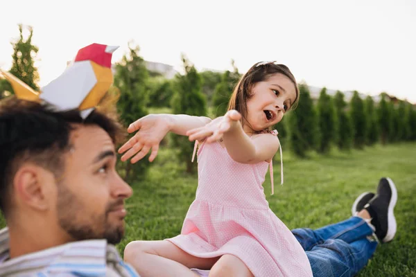 Gelukkig kind spelen met haar vader met een kleurrijke vogel speelgoed zittend op het groene gras buiten. Vrolijke dochter genieten op dag uit met haar vader in het Park. Papa en klein meisje met plezier. — Stockfoto