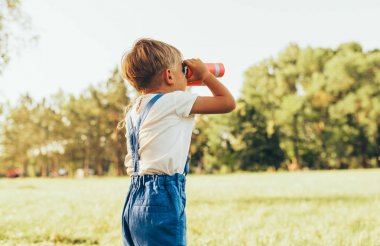 Parkta yaz günü bir hayal gücü veya keşif arayan bir dürbün ile bakarak küçük çocuk arka görüş görüntüsü. Mutlu çocuk ormanda açık havada sahte safari oyunu oynarken. Çocukluk