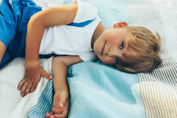 Улыбающийся очаровательный мальчик лежит на одеяле. Счастливый ребенок наслаждается летом в парке. Красивый ребенок отдыхает в лесу на солнечном свете на открытом воздухе во время пикника с родителями. Счастливого детства . — стоковое фото