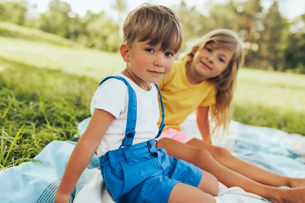 Bild von glücklichen Kindern, die auf der Decke im Freien spielen. kleiner Junge und süßes kleines Mädchen, die sich im Park entspannen. entzückende Kinder, die Spaß an der Sonne haben. Schwester und Bruder verbringen Zeit miteinander. — Stockfoto