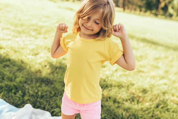 Imádnivaló szőke kislány játszik a természetben háttérben. Boldog gyermek élvezi nyáron a parkban. Vidám gyerek szórakozik az erdőben a napfény szabadban. Boldog gyerekkori. — Stock Fotó