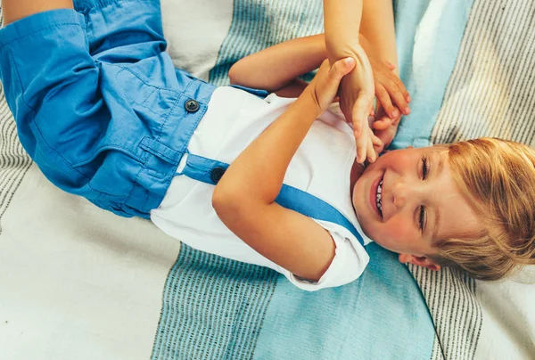Мальчик смеется и лежит на одеяле. Красивый ребенок широко улыбается и веселится на солнечном свете на открытом воздухе. Счастливый ребенок наслаждается летом в парке. Счастливого детства . — стоковое фото