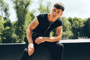 Koşudan sonra dinlenen bir atletin açık hava görüntüsü, kulaklıklardan müzik dinlemek. Spor da sert bir egzersiz sonrası rahatlatıcı genç kas erkek. İnsanlar ve spor konsepti.