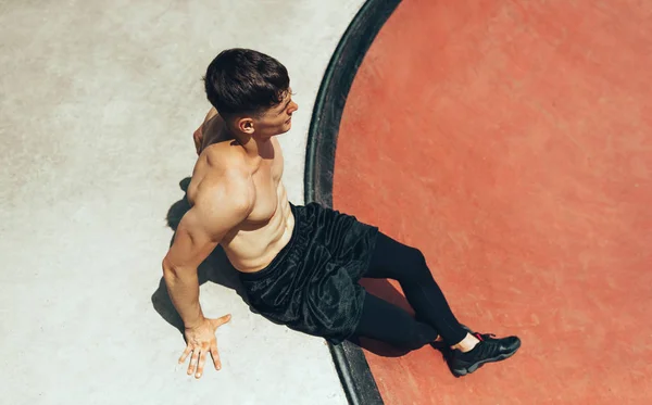 Image ci-dessus de l'athlète jeune homme musclé se reposant après l'entraînement, assis sur le terrain de sport. Homme en bonne santé et en forme prenant une pause après l'exercice à l'extérieur. Concept de personnes et de sport — Photo