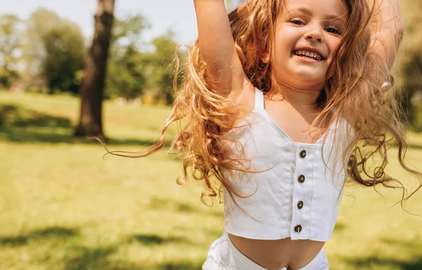 Nahaufnahme Porträt eines glücklichen kleinen Mädchens mit langen blonden Haaren, das im Hintergrund der Natur spielt. Kinder genießen die Sommerzeit im Park. fröhliche Kinder, die sich im Wald bei Sonnenlicht vergnügen. Glückliche Kindheit — Stockfoto