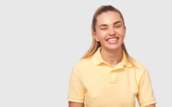 Poziome studio portret szczęśliwej pięknej pozytywnej młodej kobiety ubranej w żółty t-shirt, uśmiechając się szeroko, patrząc bezpośrednio do aparatu i stwarzające na białym tle. Ludzie i emocje — Zdjęcie stockowe