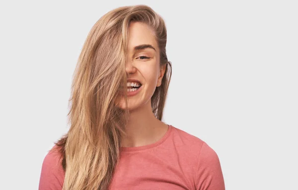 Retrato de estudio de una joven rubia feliz, con un hermoso cabello sano, sonríe positivamente vistiendo un atuendo casual y mirando a la cámara, aislada en la pared blanca del estudio. Personas emociones — Foto de Stock