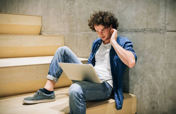 Kint kép a fiatal csípő férfi göndör haja laptop használata a beszélgető online barátokkal, csatlakozik az ingyenes vezeték nélküli a város utcán. Jóképű ember olvas az ő laptop számítógép. — Stock Fotó