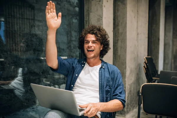 Aantrekkelijke jonge man met krullend haar met behulp van laptop voor online werken. Freelance man zittend in het café wachten zijn cliënt. Slimme mannelijke Lees nieuws, typen op zijn laptop computer in het moderne kantoor — Stockfoto