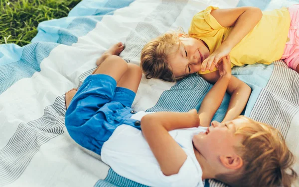 Horizontales Bild verspielter Kinder, Schwester und Bruder auf der Decke liegend, einander zuschauend. glücklicher kleiner Junge und kleines Mädchen genießen die Sommerzeit im Park. fröhliche Kinder, die draußen spielen — Stockfoto