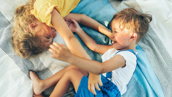 Dos adorables niños, hermana y hermano acostados en la manta, mirándose el uno al otro. Feliz niño y niña disfrutando del verano en el parque. Imagen franca de niños jugando al aire libre . — Foto de Stock