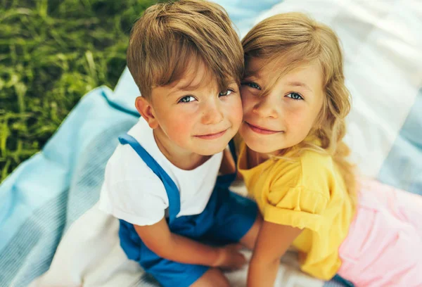 Draußen das Porträt zweier lächelnder Kinder, die draußen auf der Decke spielen. Kleiner Junge und süßes kleines Mädchen, die sich im Park zusammenschließen und entspannen. Kinder haben Spaß an der Sonne. Schwester und Bruder — Stockfoto