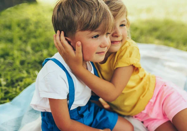 Aufrichtiges Bild von lächelnden zwei spielenden Kindern, die die Sommerzeit auf der Decke im Freien genießen. Schwester umarmt ihren kleinen Bruder im Park. Kinder haben Spaß an der Sonne. — Stockfoto