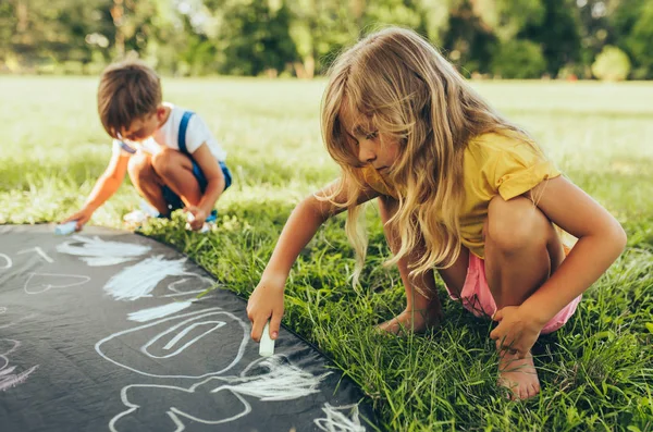 Bambini che giocano con gessetti colorati. Bambini felici che disegnano con i gessetti nel parco. Amici, ragazzo e due ragazze si divertono alla luce del sole all'aperto. Infanzia. — Foto Stock