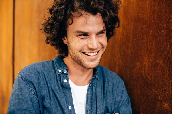 Closeup portrait of handsome young man with curly hair, smiling and looking aside, standing at modern metal building wall outdoors. Portrait of happy smart student male. People and emotion concept — Stock Photo, Image