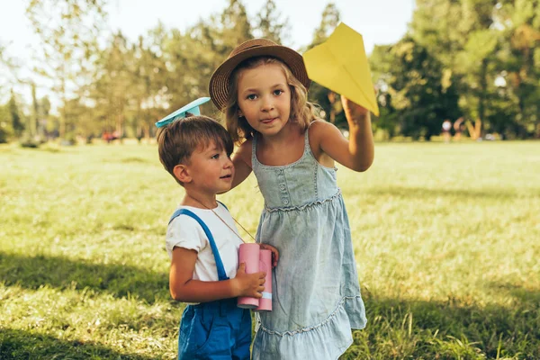 Bild von zwei Kindern, die an einem Sommertag im Park mit Fernglas und Papierflieger spielen. glückliche Schwester und Bruder spielen vorgetäuschte Safari-Spiel im Freien im Wald. Kindheitskonzept — Stockfoto