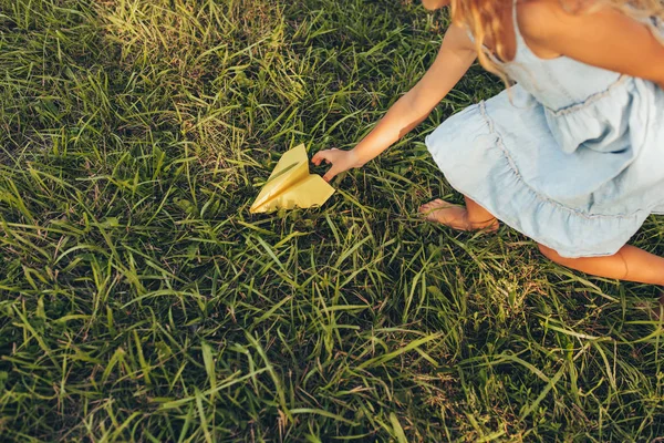 Sopra primo piano vista immagine di bambina che gioca con un aereo di carta in giorno d'estate nel parco. Un ragazzo carino che lancia un aeroplano di carta all'aperto in giardino. Concetto di infanzia — Foto Stock