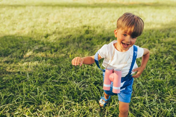 Счастливый маленький мальчик играет с биноклем в поисках воображения или исследования в летний день в парке. Активный ребенок играет и бегает по зеленой траве на открытом воздухе. Концепция детства — стоковое фото
