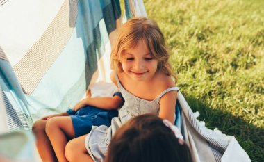 Piknik sırasında yeşil çimenler üzerinde battaniye üzerinde arkadaşlarıile oynayan küçük kız. Mutlu çocuklar eğlenmek ve parkta yaz günü zevk. Dışarıda oynayan neşeli çocuklar 
