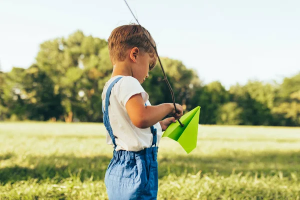 Bambino che gioca con un aereo di carta nella giornata estiva nel parco. Ragazzino che gioca all'aperto su erba verde. Concetto di infanzia — Foto Stock