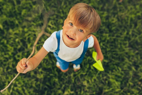 Vista dall'alto immagine di bambino carino che gioca con un aereo di carta in giornata estiva nel parco. Felice bambino sorridente e giocare all'aperto giochi su erba verde. Concetto di infanzia — Foto Stock
