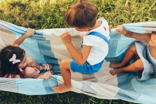 Bilder von verspielten Kindern, die gemeinsam auf der Decke auf dem grünen Rasen spielen. glücklicher kleiner Junge und kleine Mädchen genießen den Sommertag im Park. fröhliche Kinder, die draußen spielen. Kindheit — Stockfoto