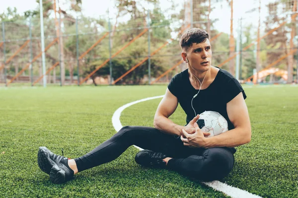Young soccer man taking a rest after training session outdoors. Healthy and fit man sitting and relaxing at green lawn after workout exercises. People and sport concept — Stock Photo, Image