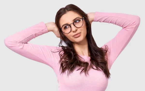 Позитивна кавказька жінка студент тримає руки на голові, озираючись в сторону, носить рожевий повсякденний одяг і круглі прозорі окуляри, ізольовані на білому фоні. — стокове фото