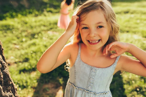 Outdoors close seup portrait of beautiful blonde little girl smiling broadly and looking to the camera in summer day in park. Милый ребенок играет с друзьями на открытом воздухе в саду. Концепция детства — стоковое фото