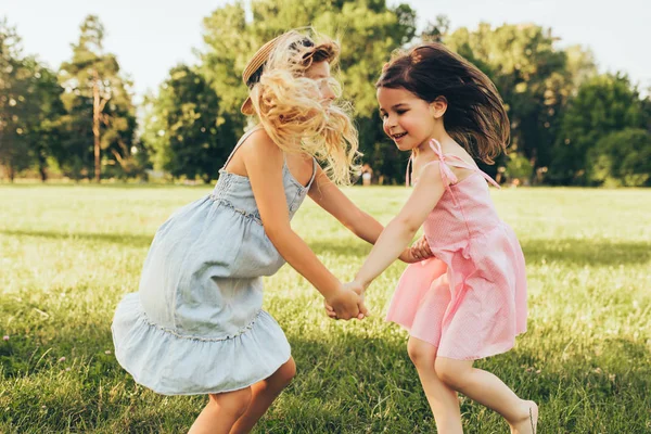Obraz dwóch małych dziewcząt taniec i grając razem na zielonej trawie w parku. Dzieci korzystające z letnich dni w parku. Dwie siostry bawią się na tle natury. Dzieciństwo i przyjaźń — Zdjęcie stockowe