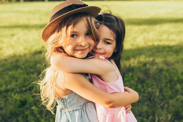 Outdoors portrait of two adorable children shares love and frienship. Two little girls playing in the park. Two sisters having fun on sunlight and nature background. Childhood and friendship concept — Stock Photo, Image