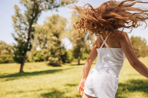 Visão traseira imagem de uma menina adorável com longos cabelos loiros dançando no fundo da natureza. Criança feliz desfrutando da hora de verão no parque. Miúdo encantador a brincar à luz do sol lá fora. Infância — Fotografia de Stock