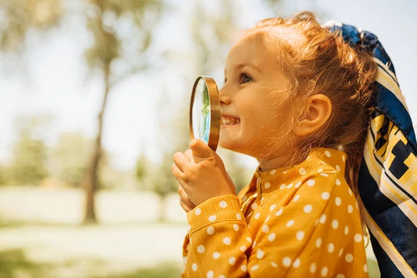 Primo piano ritratto di carina bambina felice giocare ed esplorare con lente d'ingrandimento la natura all'aperto. Bambino curioso guardando attraverso lente di ingrandimento in una giornata di sole nel parco. Infanzia. — Foto Stock