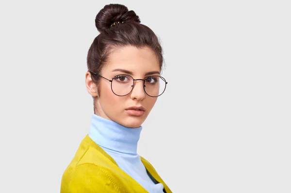 Zbliżenie studio portret poważnej młodej kobiety brunetka nosi przezroczyste okulary i strój casual, patrzy do aparatu, izolowane na białym tle. Strzał dość zmęczona kobieta na szarej ścianie — Zdjęcie stockowe