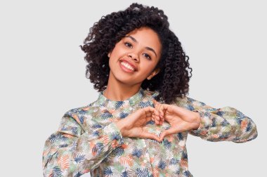 Gülümseyen genç kadın parmakları ile kalp şekil verme. Kapalı gözlerle güzel erkek pembe bluz giymiş, kalp hareketi iki el ile gösterilen, işareti, beyaz arka plan üzerinde poz seviyorum.