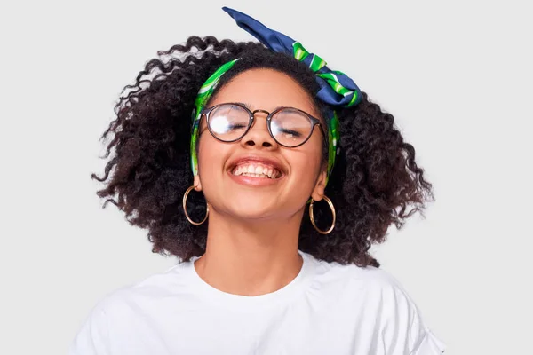 Feliz dama afroamericana sonriendo ampliamente, vistiendo camiseta blanca y gafas transparentes, disfrutar de un buen momento, posando sobre fondo de estudio blanco. Gente, éxito, emociones y concepto de felicidad —  Fotos de Stock