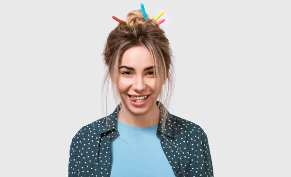 Happy young woman smiling broadly, blinking with an eye, showing tongue while looking to the camera, standing against white studio background. — Stock Photo, Image